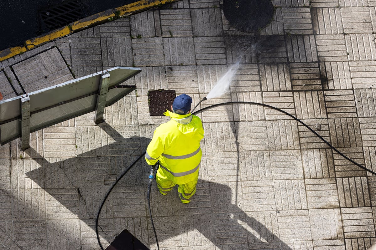 Worker cleaning a sidewalk with a high pressure water jet machine